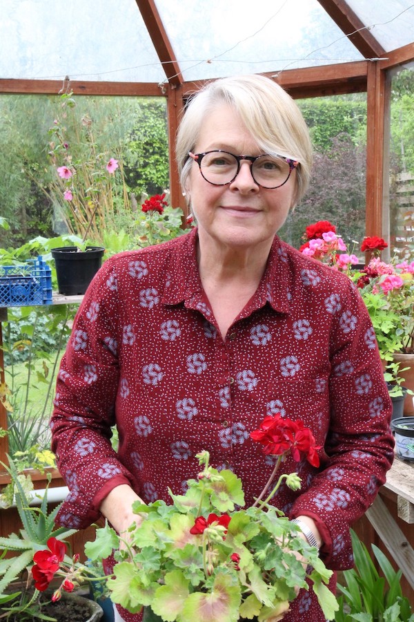 A photo of Kate holding two plants in her garden